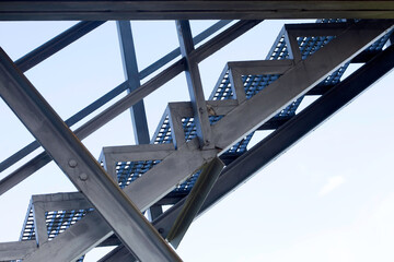 Iron staircase for up to maintenance work. Steel framing and beams structural elements against blue sky from low point of view.