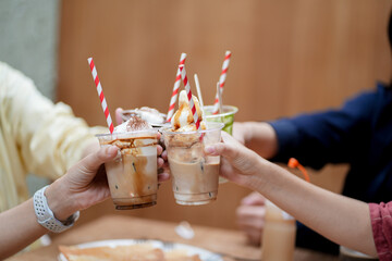 Hands of teenage girls holding glass of ice coffee together at cafe.