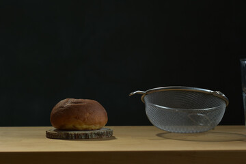 Bread roll and flour sifter placed on wood counter bar.