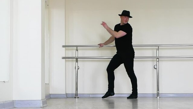 Jazz dance or caberet rehearsal in the studio by a young guy in a gangster hat. Creative dance blues mena. A dancer in black clothes makes beautiful swings with his legs