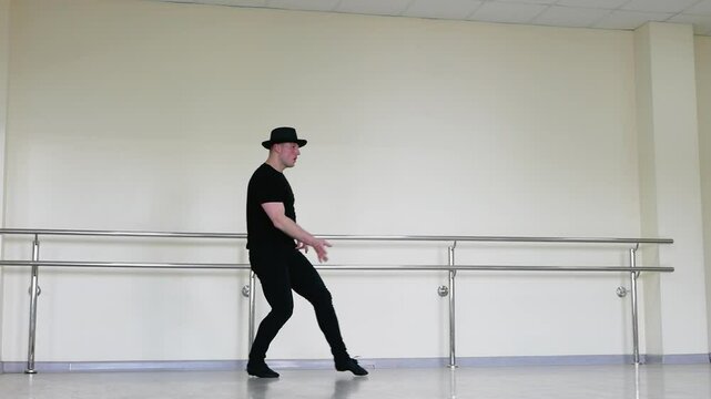 A set of fast dance moves. Jas men dances in the studio. A male dancer in a hat and a black suit and jazz shoes