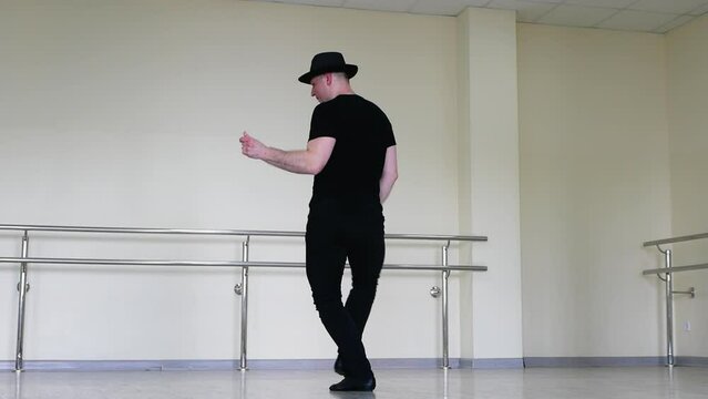 Jazz dance or caberet rehearsal in the studio by a young guy in a gangster hat. Creative dance blues mena. Dancer in black clothes against the background of a mirror in reflection