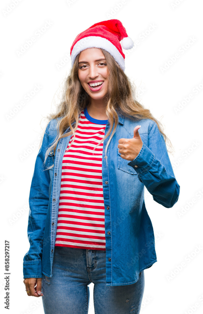 Sticker beautiful young blonde woman wearing christmas hat over isolated background doing happy thumbs up ge