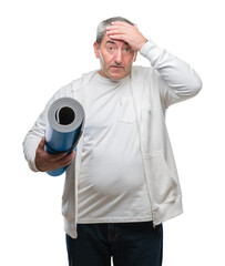 Handsome senior man holding yoga mat over isolated background stressed with hand on head, shocked with shame and surprise face, angry and frustrated. Fear and upset for mistake.