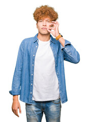 Young handsome man with afro hair wearing denim jacket mouth and lips shut as zip with fingers....