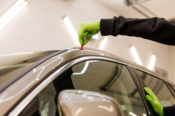 Person in green gloves repairing vehicle, working on car hood