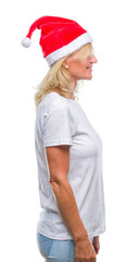 Middle age blonde woman wearing christmas hat over isolated background looking to side, relax profile pose with natural face with confident smile.