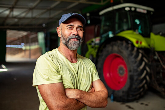 Confident male farmer with arms crossed standing in tractor shed