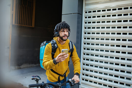 Delivery man checking smartphone while standing with bicycle on city street