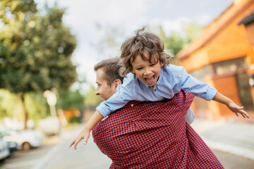 Joyful father giving piggyback ride to son on suburban street