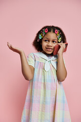A cute African American girl with hair clips stands in a rainbow-colored dress, smiling at the camera.
