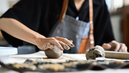 A close-up of a person's hands shaping clay on a worktable, highlighting the artistic and creative...