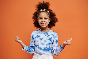 Young African American girl smiling in blue and white tie-dye shirt and hair clips on orange...