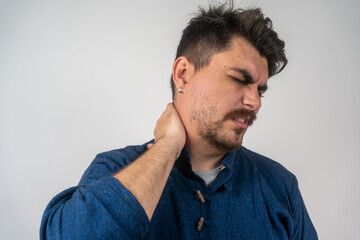 Obraz premium Young handsome man in blue shirt, touching his neck because it hurts after long working hours, feeling exhausted and worried, isolated on gray background