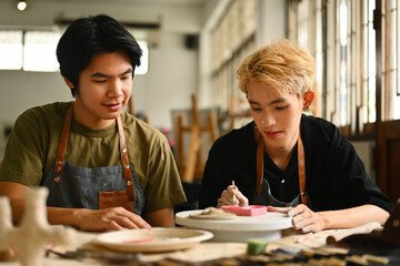 An art instructor observes and guides an LGBT student as they paint a ceramic piece. Both are...