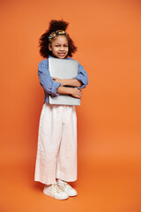 A young African American girl in a trendy outfit and hair clips stands confidently against an...