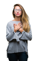 Young beautiful blonde woman wearing glasses over isolated background smiling with hands on chest with closed eyes and grateful gesture on face. Health concept.