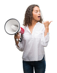 Young hispanic woman holding megaphone pointing and showing with thumb up to the side with happy face smiling