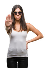 Young beautiful hispanic wearing sunglasses doing stop sing with palm of the hand. Warning expression with negative and serious gesture on the face.