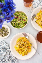 Stewed rice with chicken breast and mixed salad with radishes and various seeds, a served table with food and a vase of flowers, a delicious hearty lunch or dinner