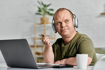 A man with inclusivity wearing headphones sits at his desk in his home office working.