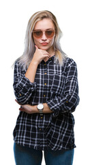 Naklejka premium Young blonde woman wearing sunglasses over isolated background with hand on chin thinking about question, pensive expression. Smiling with thoughtful face. Doubt concept.