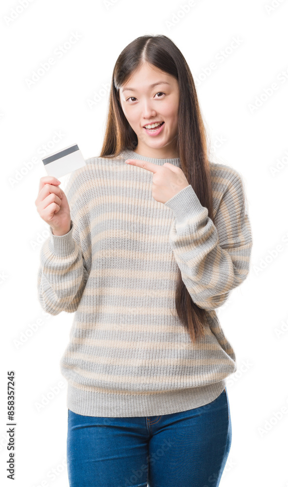 Poster Young Chinese woman over isolated background holding credit card very happy pointing with hand and finger