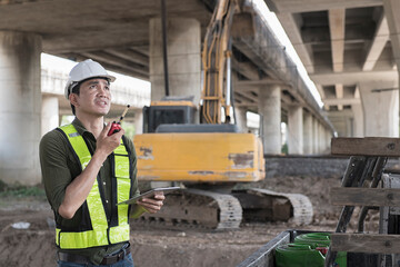 Male Civil Engineer Talking radio communication  and Using Tablet On Construction Site of New road. Discussing Business, Excavators Working.