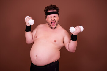 Fitness and healthy lifestyle. A funny fat man is doing sports. Brown background.