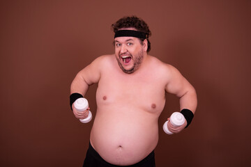 Fitness and healthy lifestyle. A funny fat man is doing sports. Brown background.