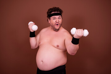Fitness and healthy lifestyle. A funny fat man is doing sports. Brown background.