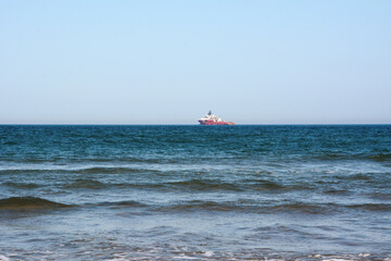 A large ship sails in the sea far on the horizon on a bright cloudless day
