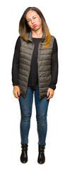 Beautiful middle age woman wearing winter vest puffing cheeks with funny face. Mouth inflated with...