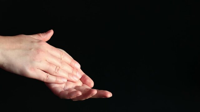 Woman applying hand cream, black background. Moisturizing cream for skin. Anti-aging cosmetics. Feminine hand care. Girl applying hand cream to the skin using massage movements