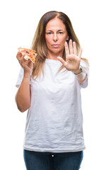 Middle age hispanic woman eating pizza slice over isolated background with open hand doing stop sign with serious and confident expression, defense gesture