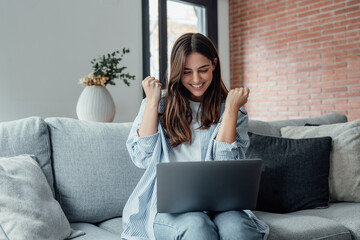 Excited emotional screams with joy woman sit on sofa hold on lap notebook makes Yes hand gesture...