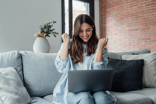 Excited emotional screams with joy woman sit on sofa hold on lap notebook makes Yes hand gesture feels happy getting job of dream, e-mail sales discount special offer, on-line lottery victory concept.
