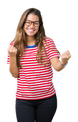 Young beautiful brunette woman wearing glasses and stripes t-shirt over isolated background very happy and excited doing winner gesture with arms raised, smiling and screaming for success. Celebration