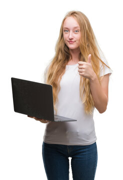 Blonde teenager woman using computer laptop happy with big smile doing ok sign, thumb up with fingers, excellent sign