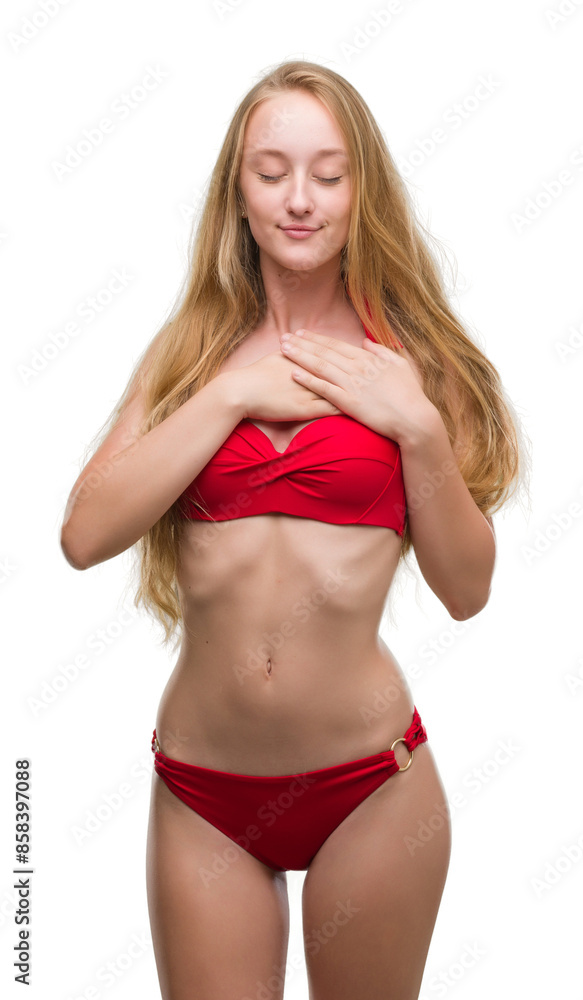 Poster Blonde teenager woman wearing red bikini smiling with hands on chest with closed eyes and grateful gesture on face. Health concept.