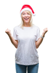 Young beautiful blonde woman wearing christmas hat over isolated background celebrating surprised and amazed for success with arms raised and open eyes. Winner concept.