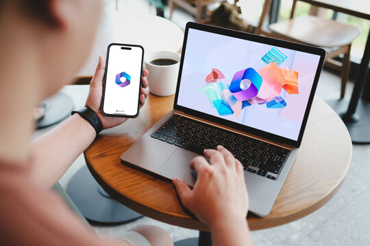 Bangkok. Thailand. JUNE 20,2024 :A man useing laptop computer and phone displaying logos of Microsoft 365, a product family of productivity software and cloud-based services owned by Microsoft.