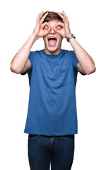 Naklejka premium Young handsome man wearing blue t-shirt over isolated background doing ok gesture like binoculars sticking tongue out, eyes looking through fingers. Crazy expression.