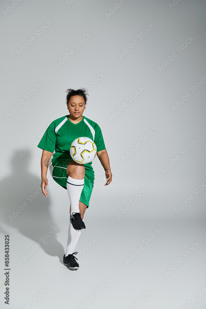 Wall mural A woman in a green jersey skillfully juggles a soccer ball in a studio setting.