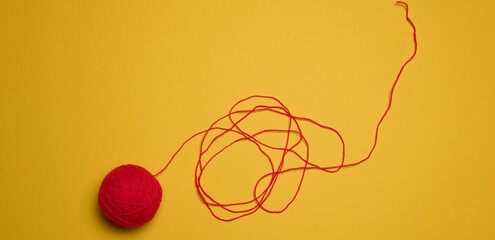 A ball of red woolen threads on a yellow background