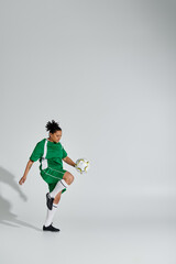 A woman in a green soccer uniform juggles a white ball in a studio setting.