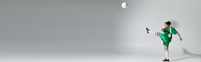 A woman in a green soccer uniform kicks a ball with her right leg, mid-air, in a studio setting.