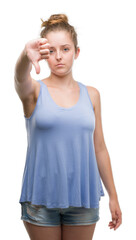 Young blonde woman looking unhappy and angry showing rejection and negative with thumbs down gesture. Bad expression.