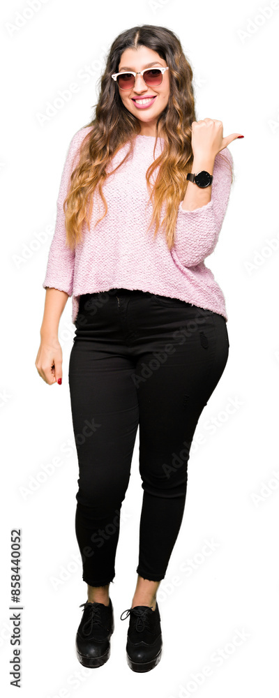 Sticker Young beautiful woman wearing sunglasses and pink sweater smiling with happy face looking and pointing to the side with thumb up.