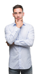 Handsome young businessman looking confident at the camera with smile with crossed arms and hand raised on chin. Thinking positive.